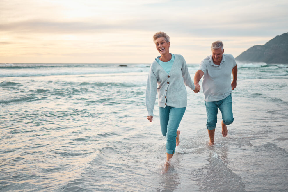 Beach, walking and senior couple holding hands for support, love and care with outdoor wellness, retirement and holiday lifestyle with sunset sky. Elderly people running together in sea ocean water.
