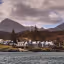 The image is well-composed with a balanced view of the coastal architecture against a mountainous backdrop. It features excellent natural lighting that highlights the textures of the landscape and building, and it is sharp throughout, maintaining clear detail in both the foreground water and the distant peaks. The colors are natural and accurate to a realistic outdoor setting. There are no unwanted elements such as watermarks, clutter, or poor composition present.